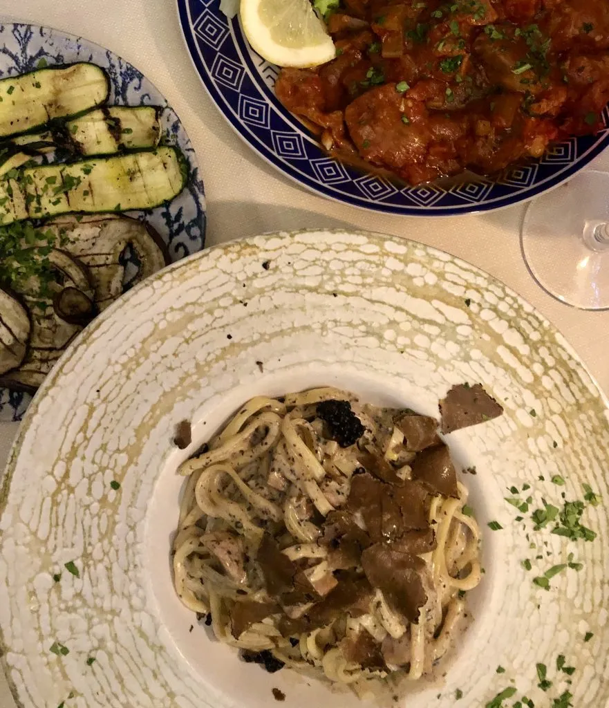 pasta, meat dish, and grilled vegetables grouped together on the table at a restaurant in italy