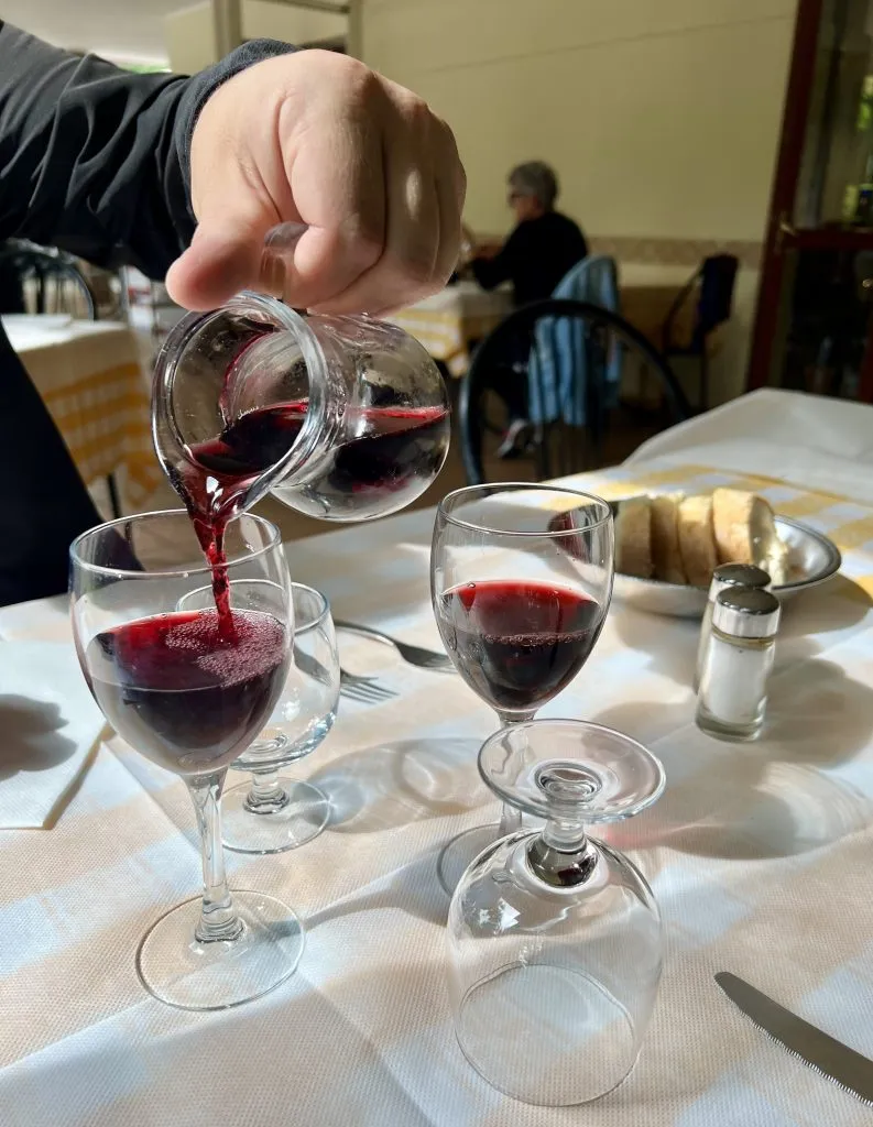hand pouring vino della casa into 2 glasses when dining in italy restaurant