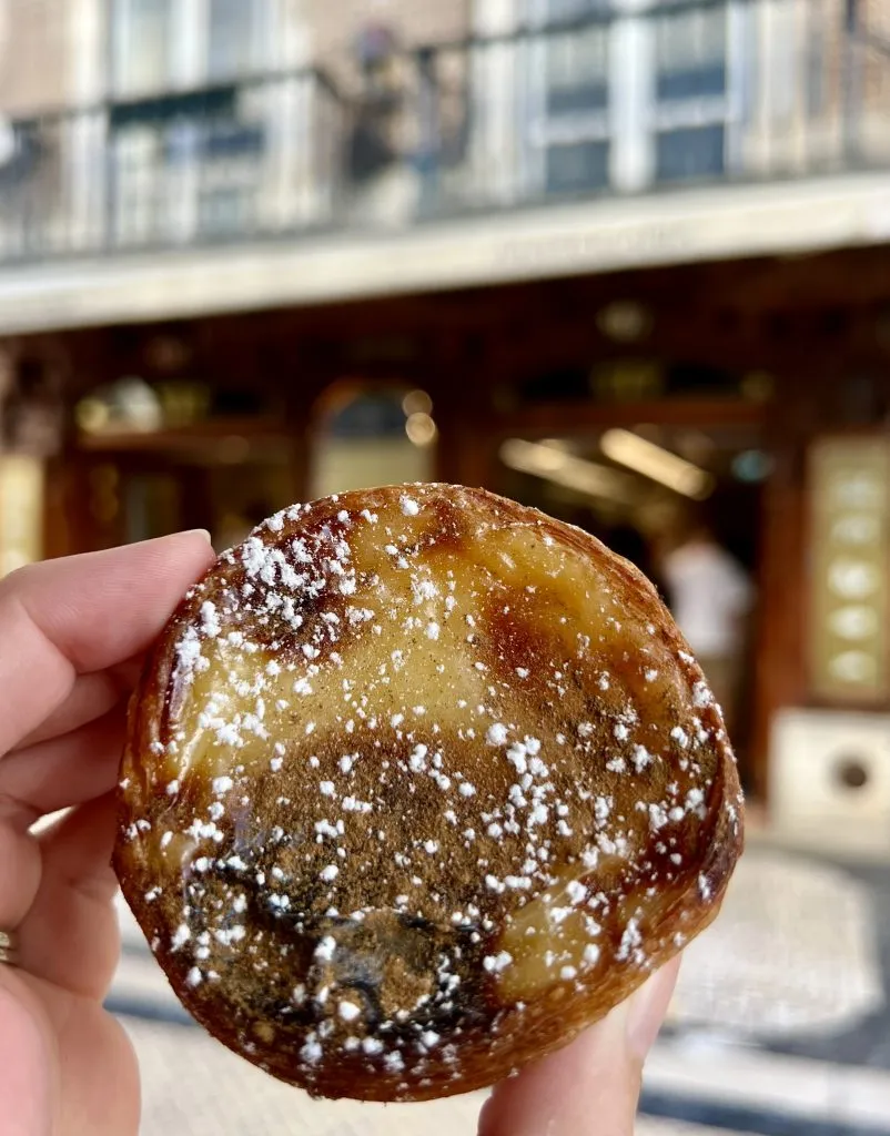pastel de nata from Manteigaria being held up in front of baixa storefront