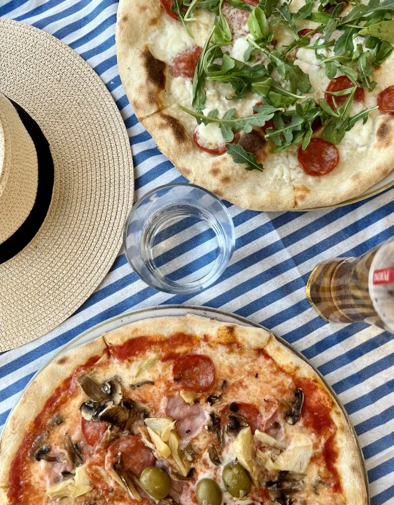 flatlay of 2 pizzas in italy restaurant with a sunhat and beer