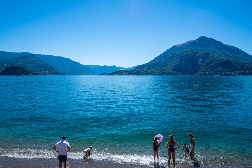 travelers along the edge of bellagio lake como preparing to swim