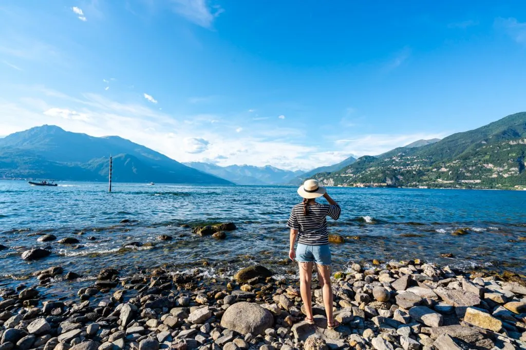 kate storm in shorts and a sunhat overlooking lake como from a rocky beach
