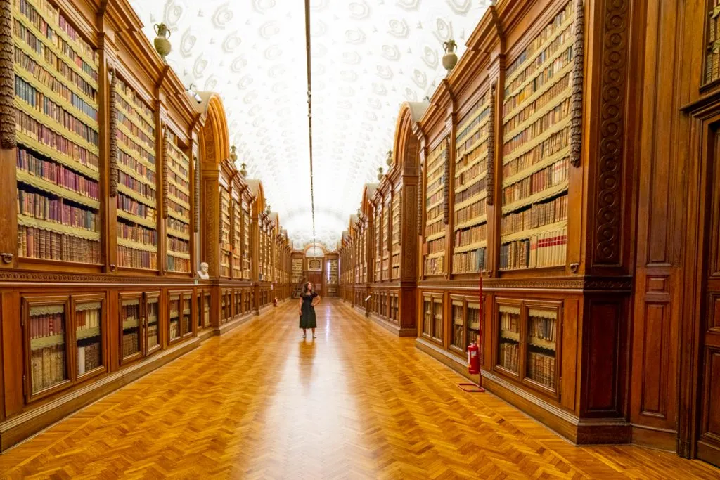 kate storm standing inside the biblioteca palatina when visiting parma italy, with bookshelves on both sides of the image