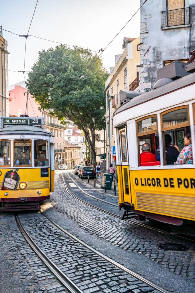 2 yellow trams passing each other on a cobbled street as seen when visiting lisbon portugal