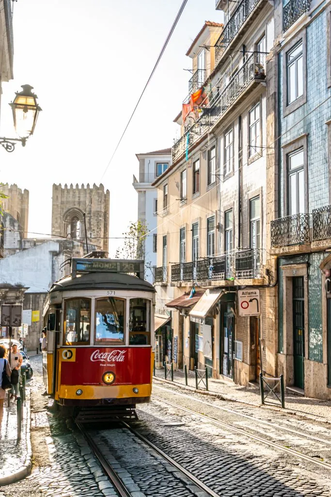 lisbon tram with tiled buildings to the right and cathedral behind it
