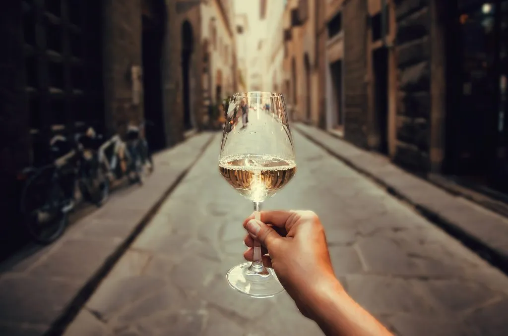 person holding out a glass of white wine on one of the cobbled streets of rome