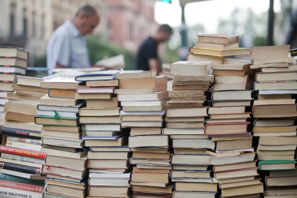 pile of books for sale as things to buy in rome italy, two men reading in the background