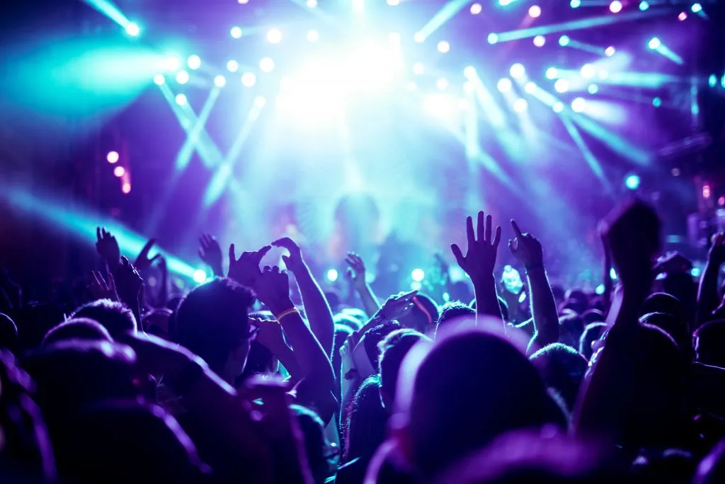 crowd raising their hands in a club with bright lights, madrid nightlife is legendary