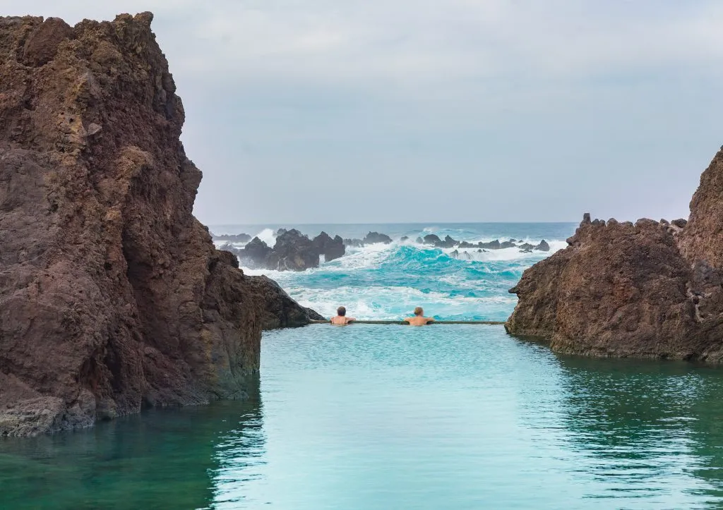 two people swimming in natural swimming pools in porto moniz madeira, one of the best portugal beach towns