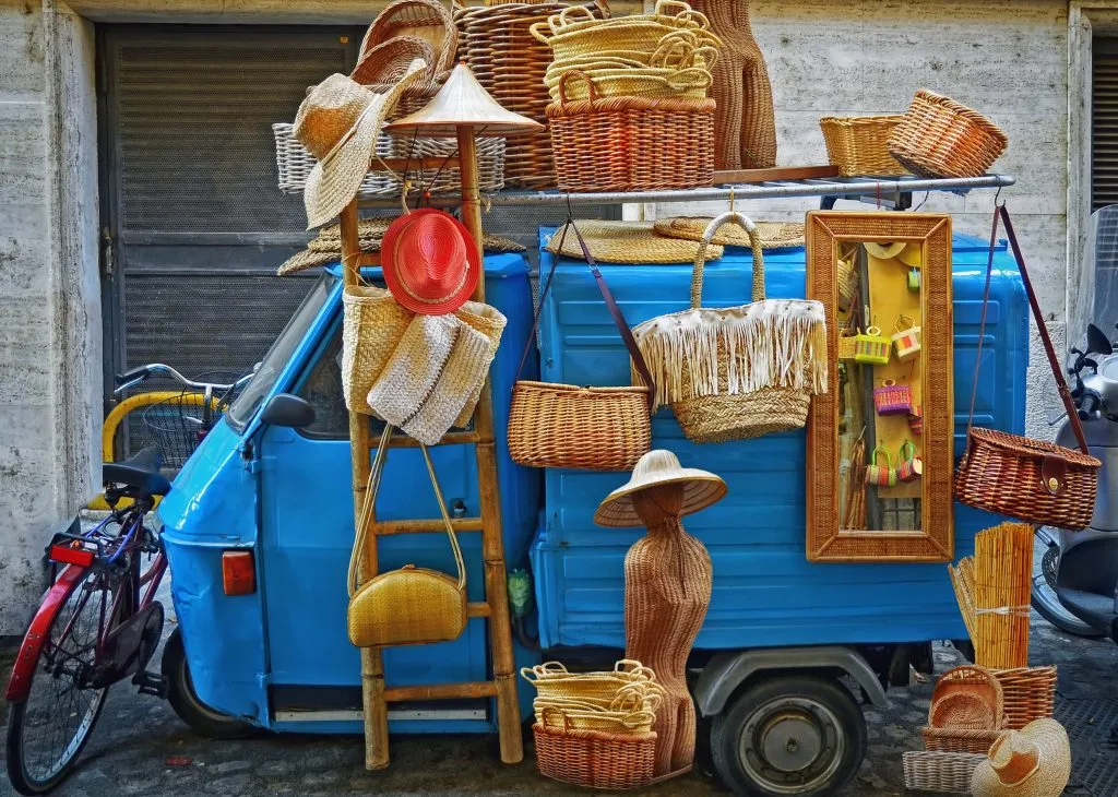 baskets and other handicrafts for sale at rome market with blue ape behind them