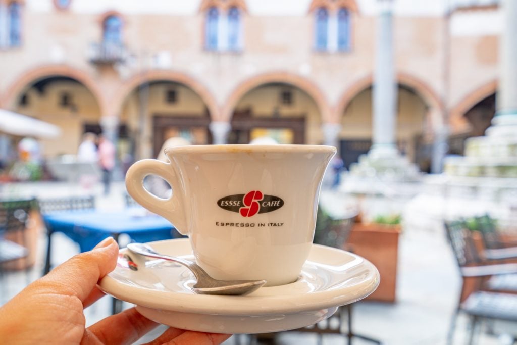 coffee cup being held up in front of the piazza del popolo, one of the best places to visit in ravenna italy