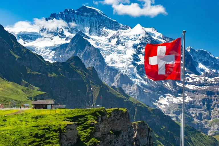 swiss flag in front of the snowy alps at mannlichen in jungfrau region, one of the most beautiful places to visit in switzerland