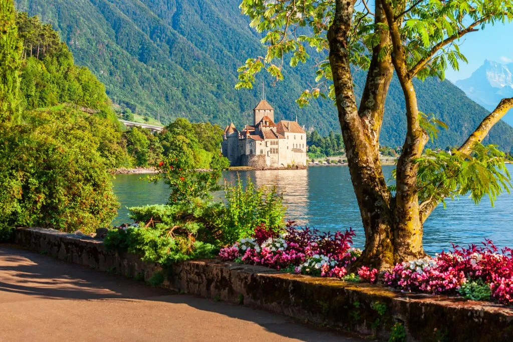 Château de Chillon as seen from across lake geneva with a path and flowers in the foreground