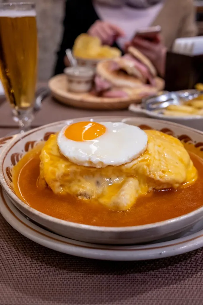 francesinha served in portugal with other food in the background