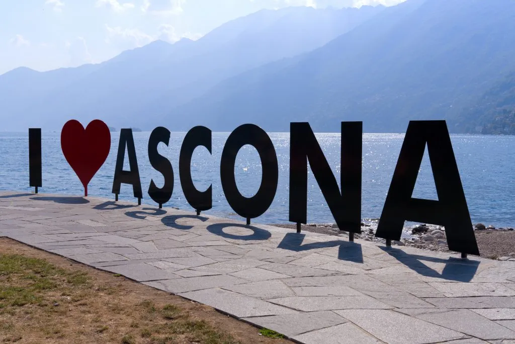 black and red sign reading "i heart ascona" near lake shore