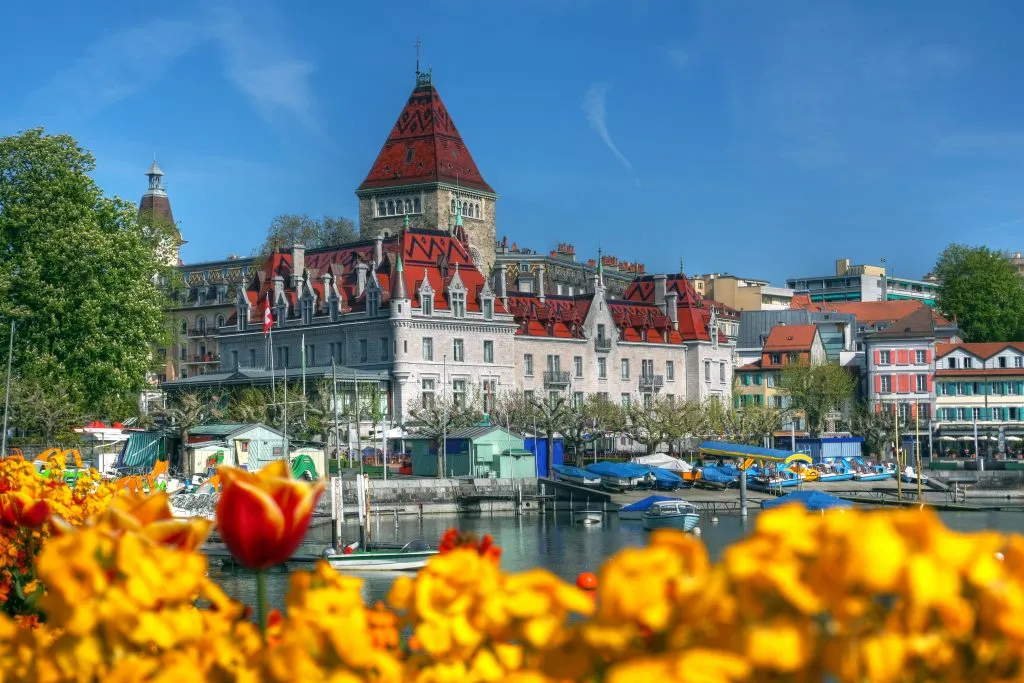 view of chateau in lausanne with flowers and lake in the foreground, one of the best switzerland cities to visit