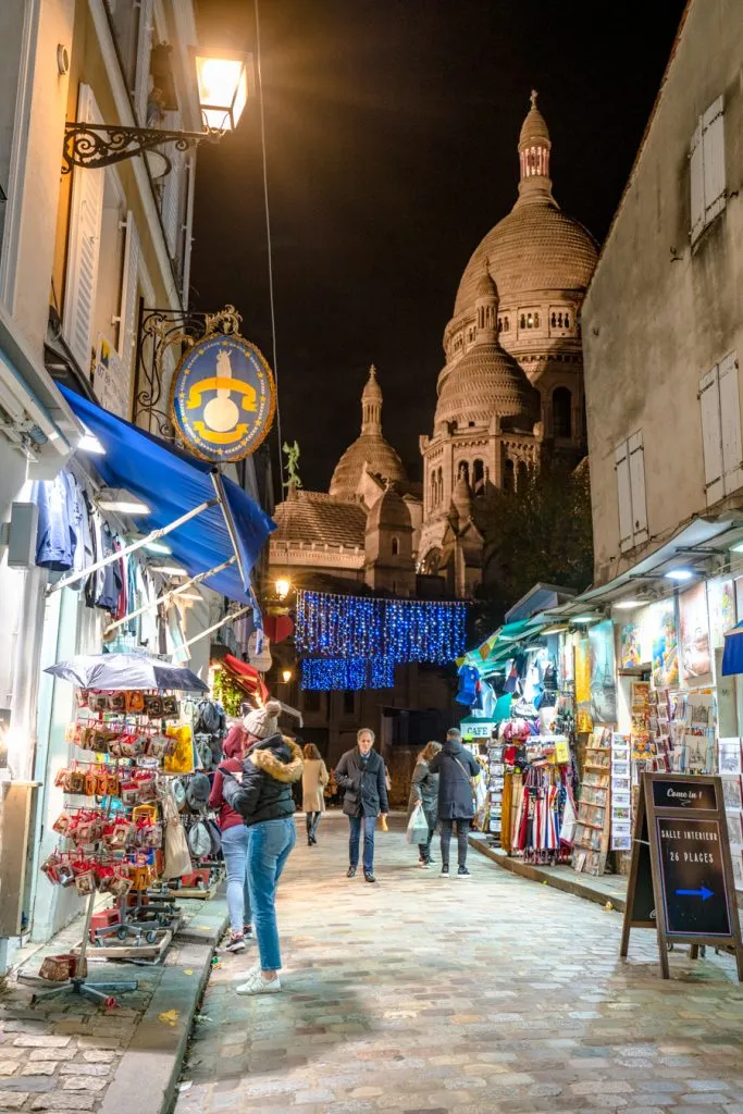view of shopping street in montmartre at night with sacre coeur domes in the background