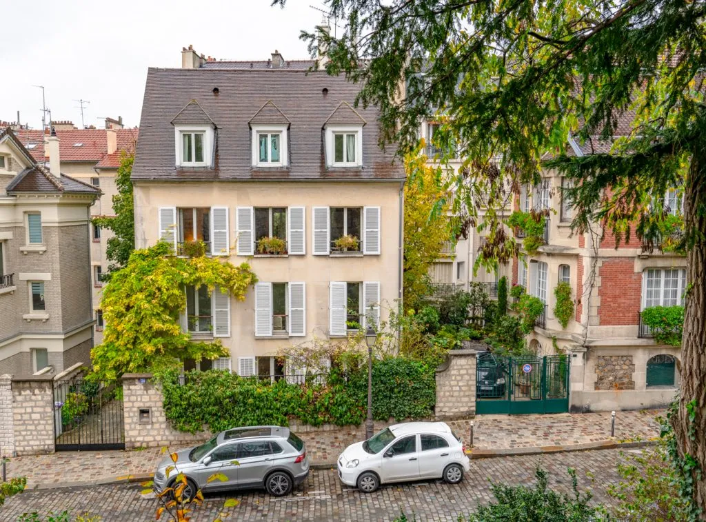 view of pretty houses and 2 cars parked on a cobblestone street in 18th arrondissement montmartre