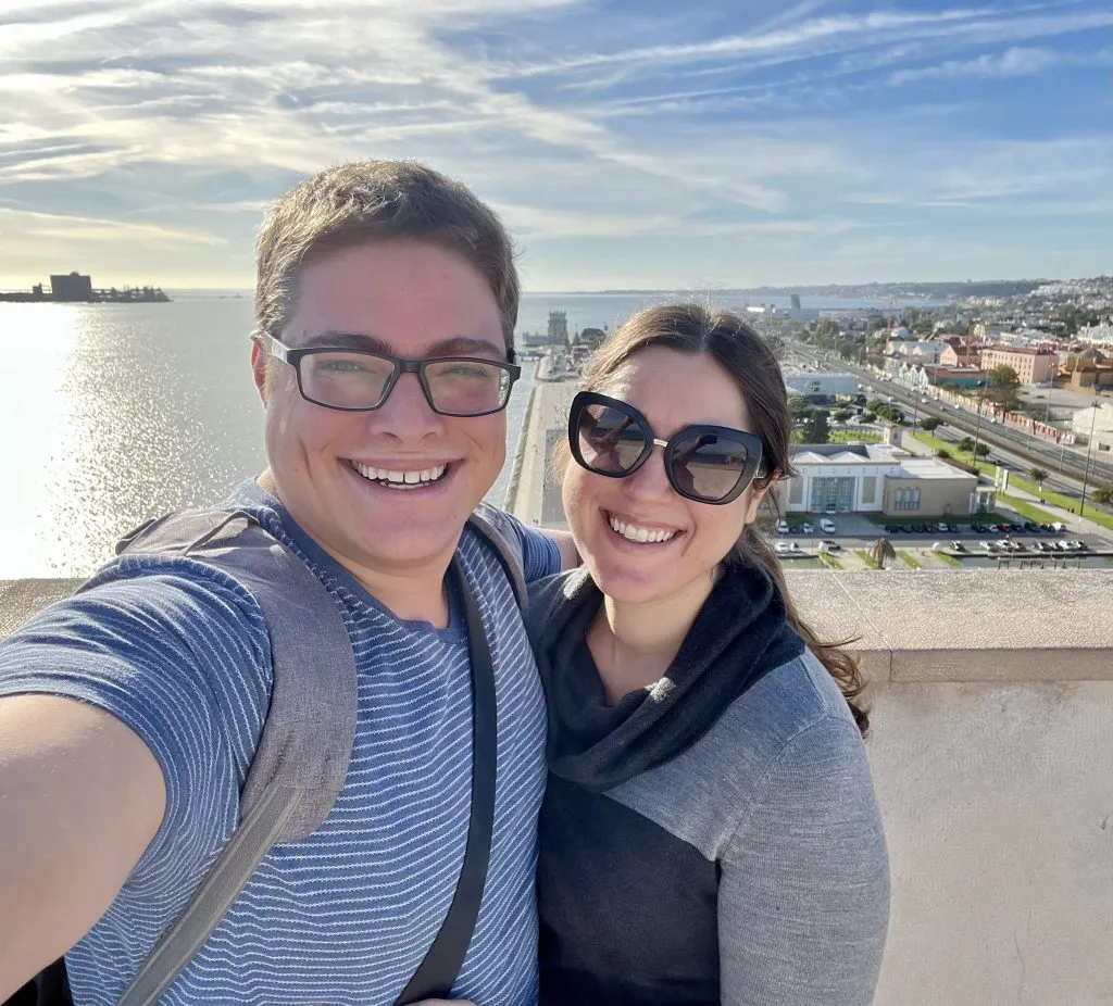 kate storm and jeremy storm taking a selfie at the top of the monument to the discoveries with tagus river visible in the background