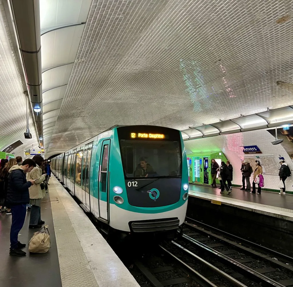 paris metro train pulling into a busy station with a white tiled ceiling
