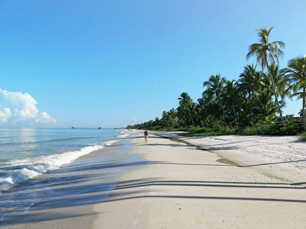 person in the distance walking down a beach in naples florida, one of the best places to visit in summer in america