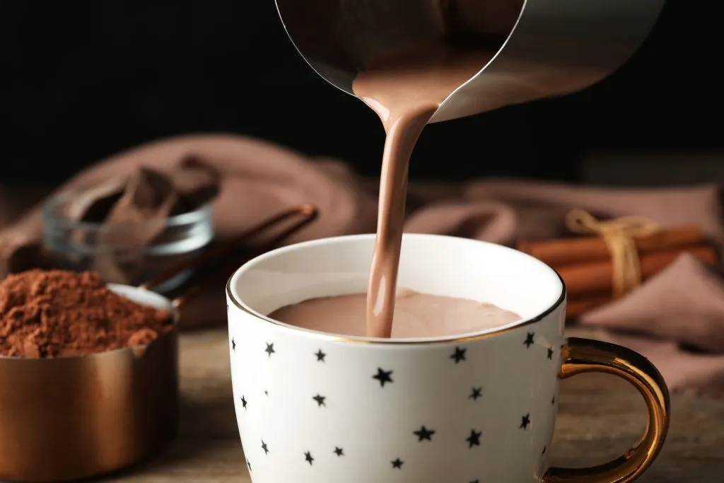 hot chocolate being poured into a mug with chocolate mix in the background