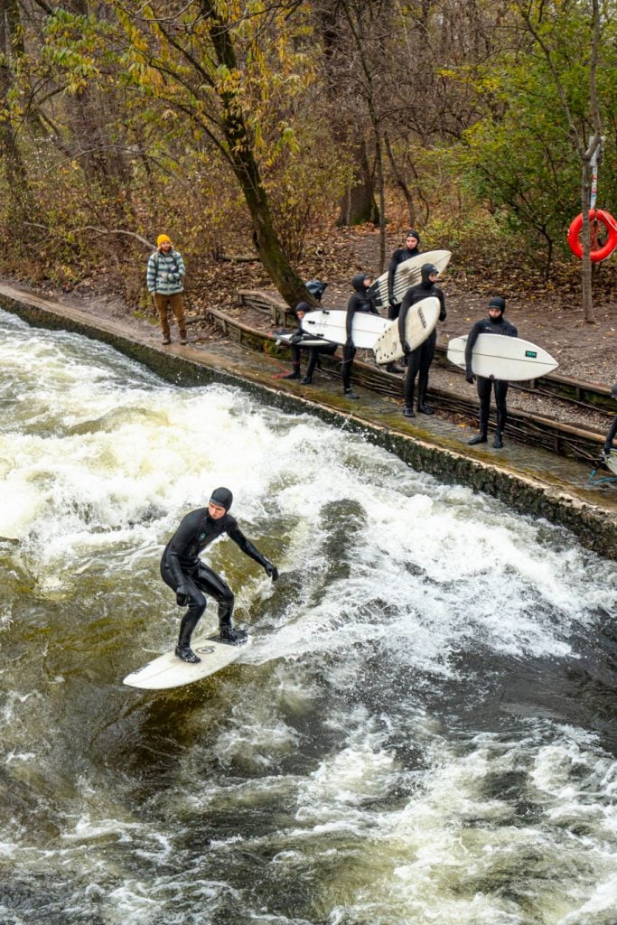 man in a wet suit river surfing at Eisbachwelle in munich in winter