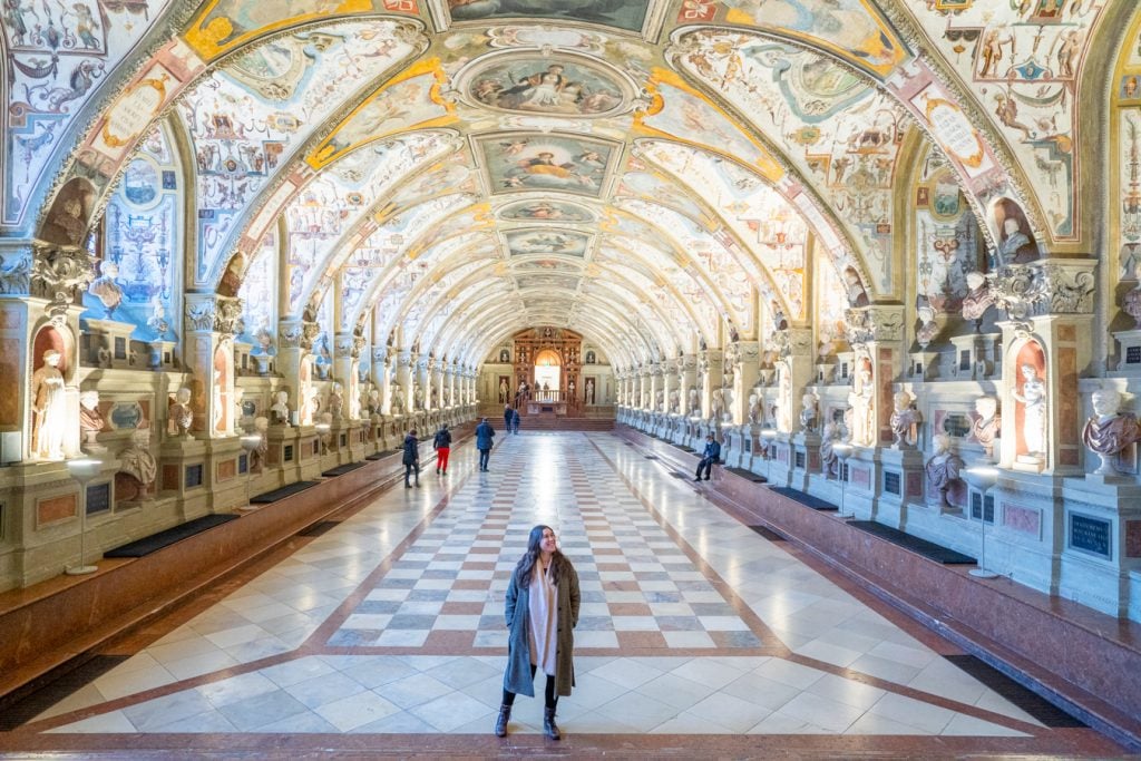 kate storm in the munich residenz wearing a voat and scarf