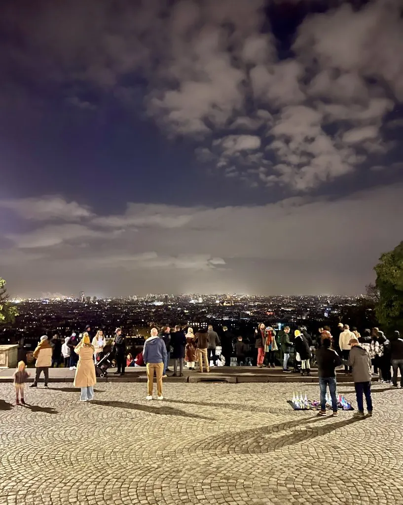 crowd of people enjoying the steps of sacre coeur overlooking paris at night