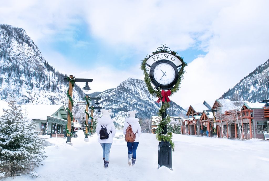 two people walking through downtown frisco past a clock on a snowy day, frisco is one of the prettiest colorado mountain towns