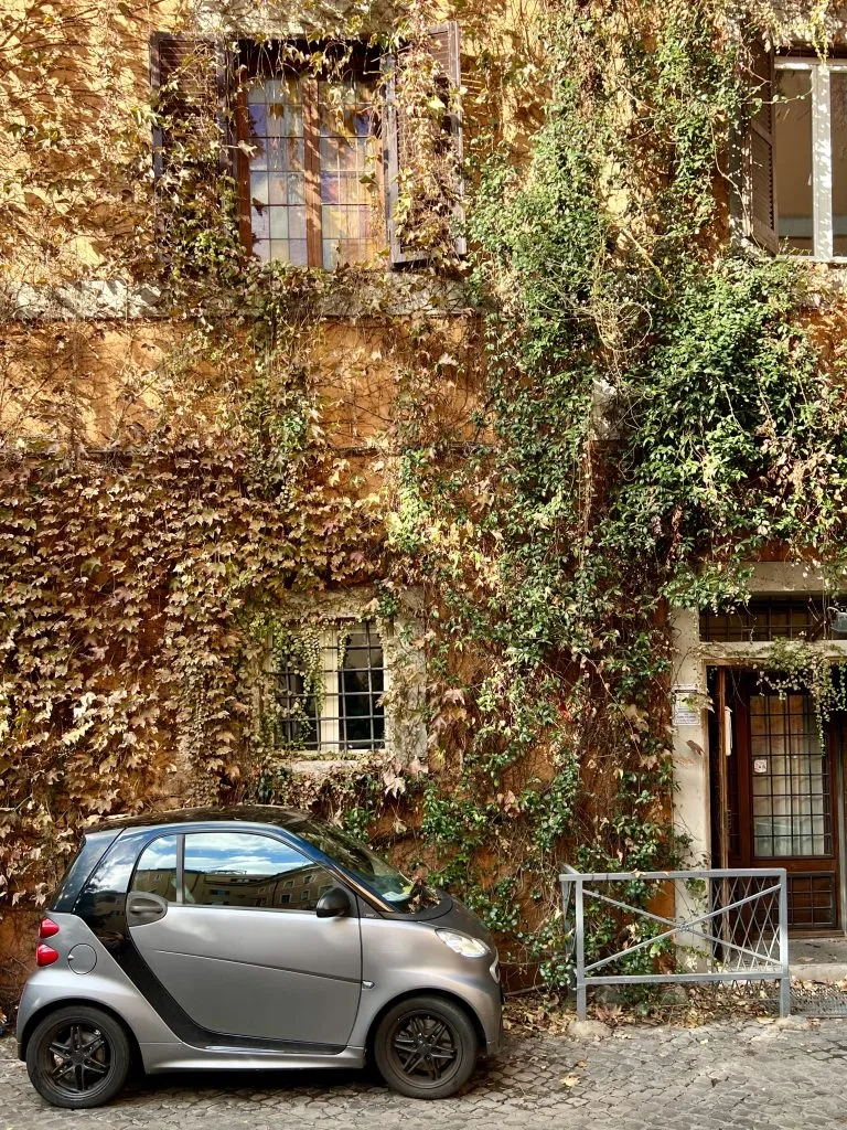 building covered in ivy with a small silver car parked out from as seen when exploring the prettiest streets in trastevere travel guide