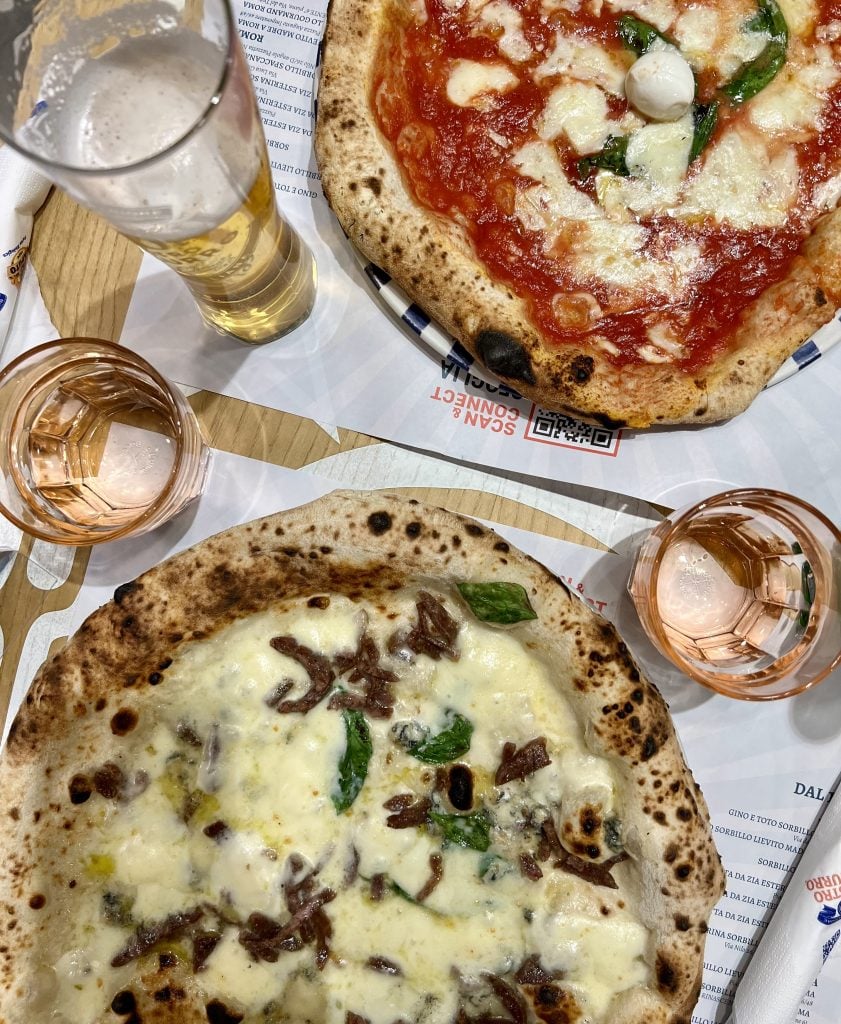 two neapolitan style pizzas shot from above with a beer on the table, guide to how to eat pizza in italy
