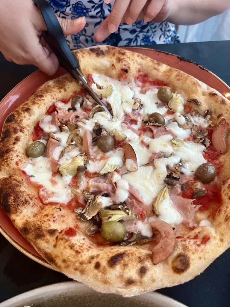 kate storm slicing a capricciosa traditional italian pizza with scissors