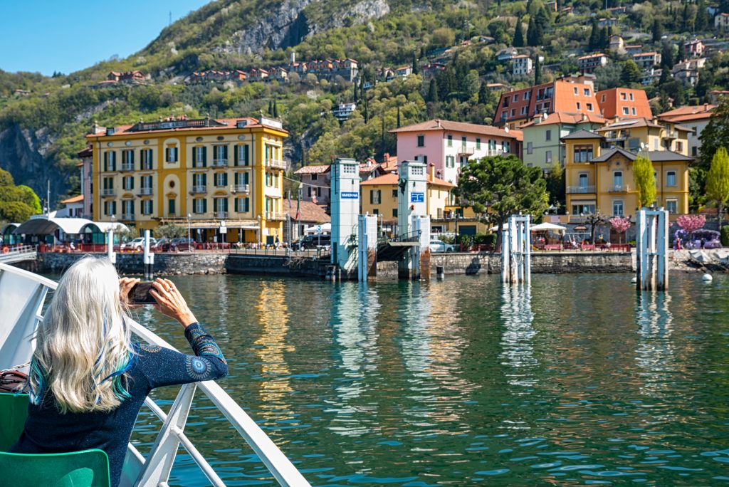 view of varenna from lake como ferry with a woman taking a photo of the town