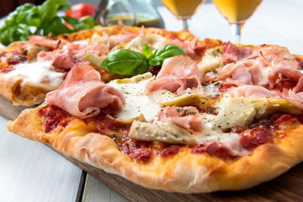 pizza alla pala on a table with greens and 2 drinks