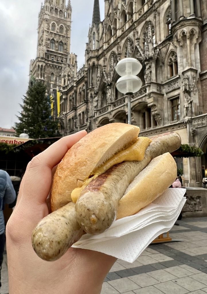 munich white sausage on a bun being held up in front of a bavaria christmas market