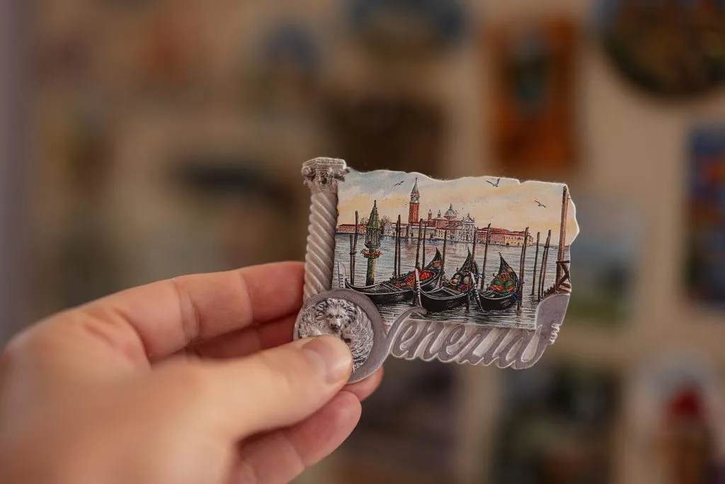 person holding out a fridge magnet that says "venezia" and shows gondolas, one of the best venice souvenirs to buy
