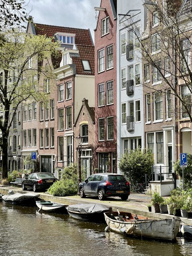 rowhouses in front of a canal in amsterdam with small boats parked in front