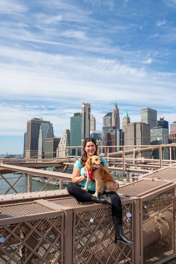 kate storm sitting on the brooklyn bridge with her dog ranger storm, manhattan skyline behind her