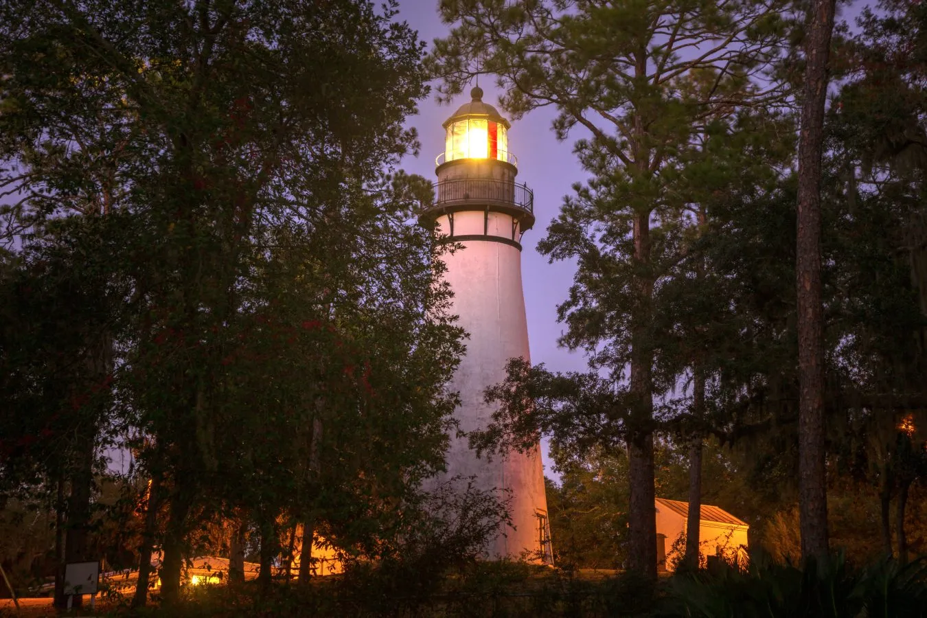 amelia island lighthouse lit up at night, as seen through trees in one of the best east coast beach towns