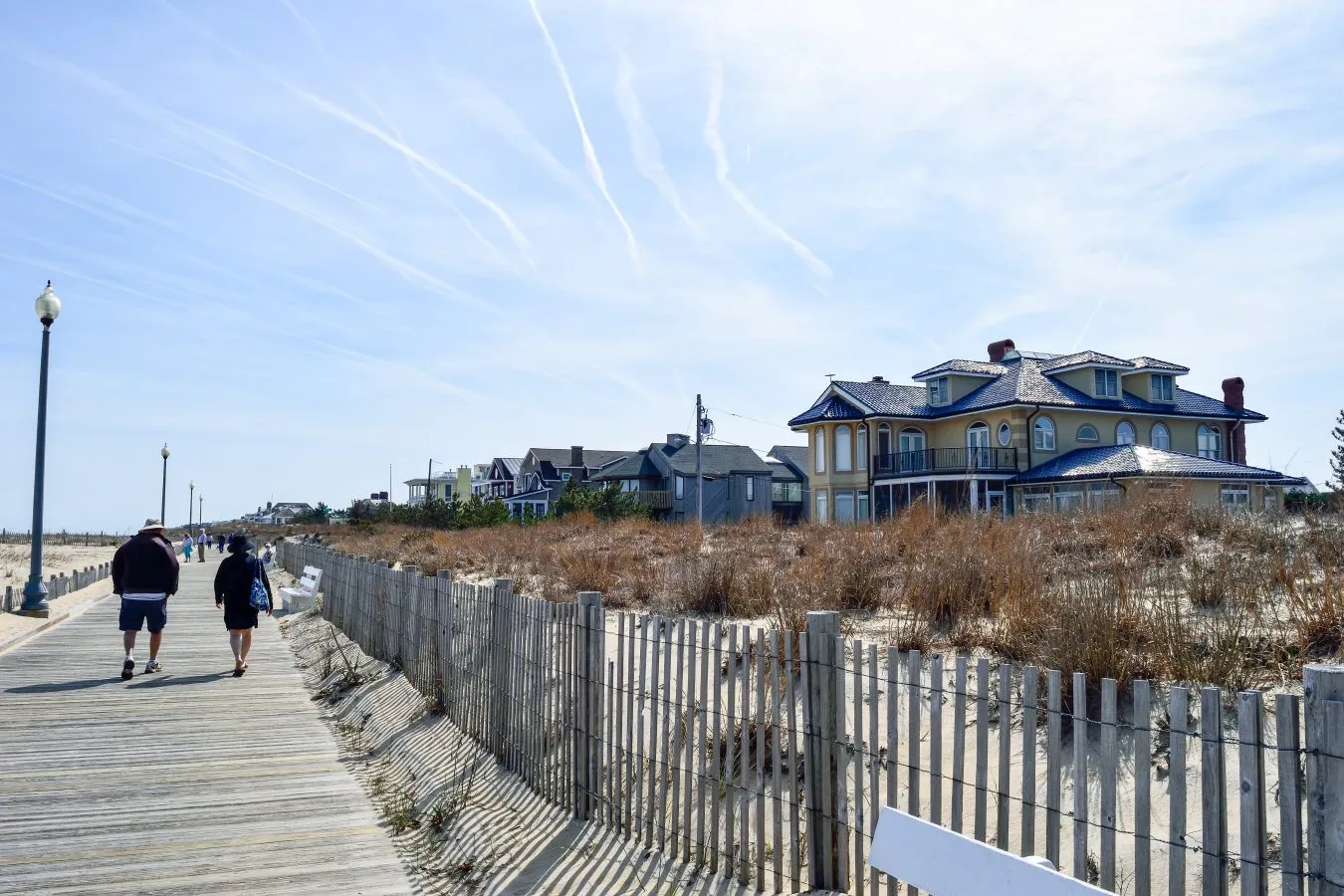two people walking along a wooden boardwalk at the beach in rehoboth beach with beach houses visible to the right