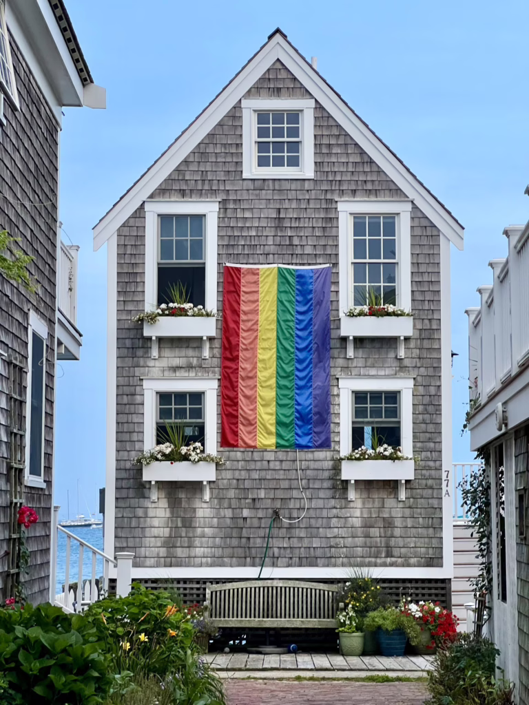 classic wooden house in provincetown ma with a pride flag hanging out front, one of the best towns in new england to visit