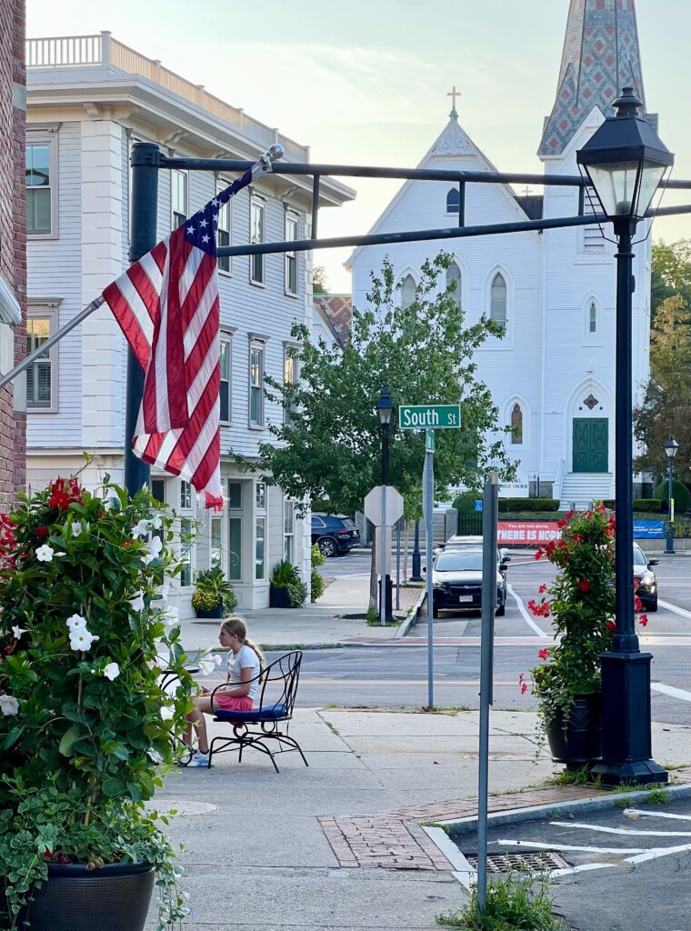 downtown hingham ma seen from sidewalk, with american flag in the foreground and white wood church in the background
