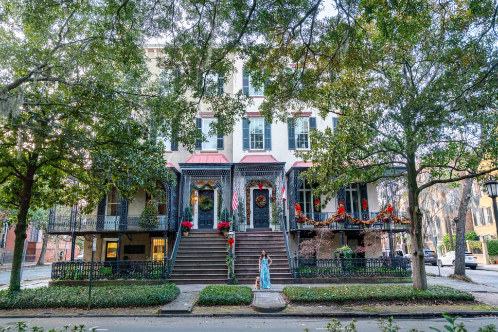 kate storm and ranger storm standing in front of two houses in the savannah historic district, decorated for christmas when visiting savannah in winter